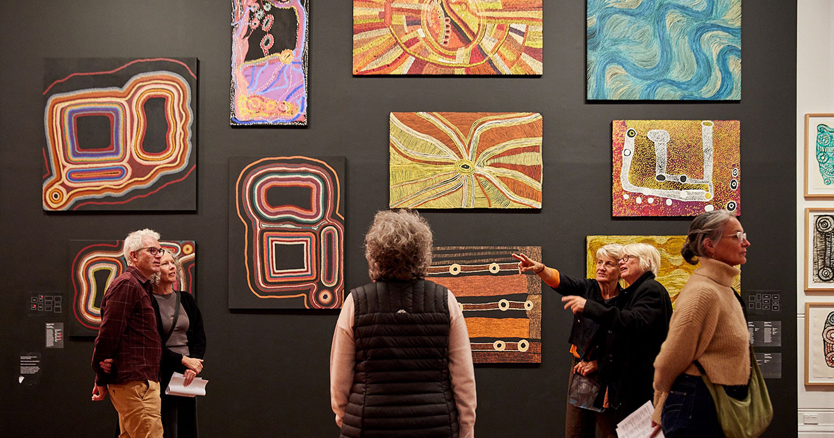 A small group of people looking at Aboriginal art works on the wall in an art gallery