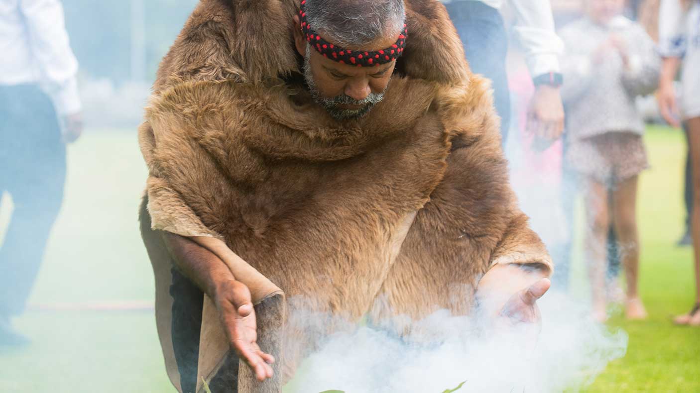 An Aboriginal man in traditional dress performing a smoking ceremony