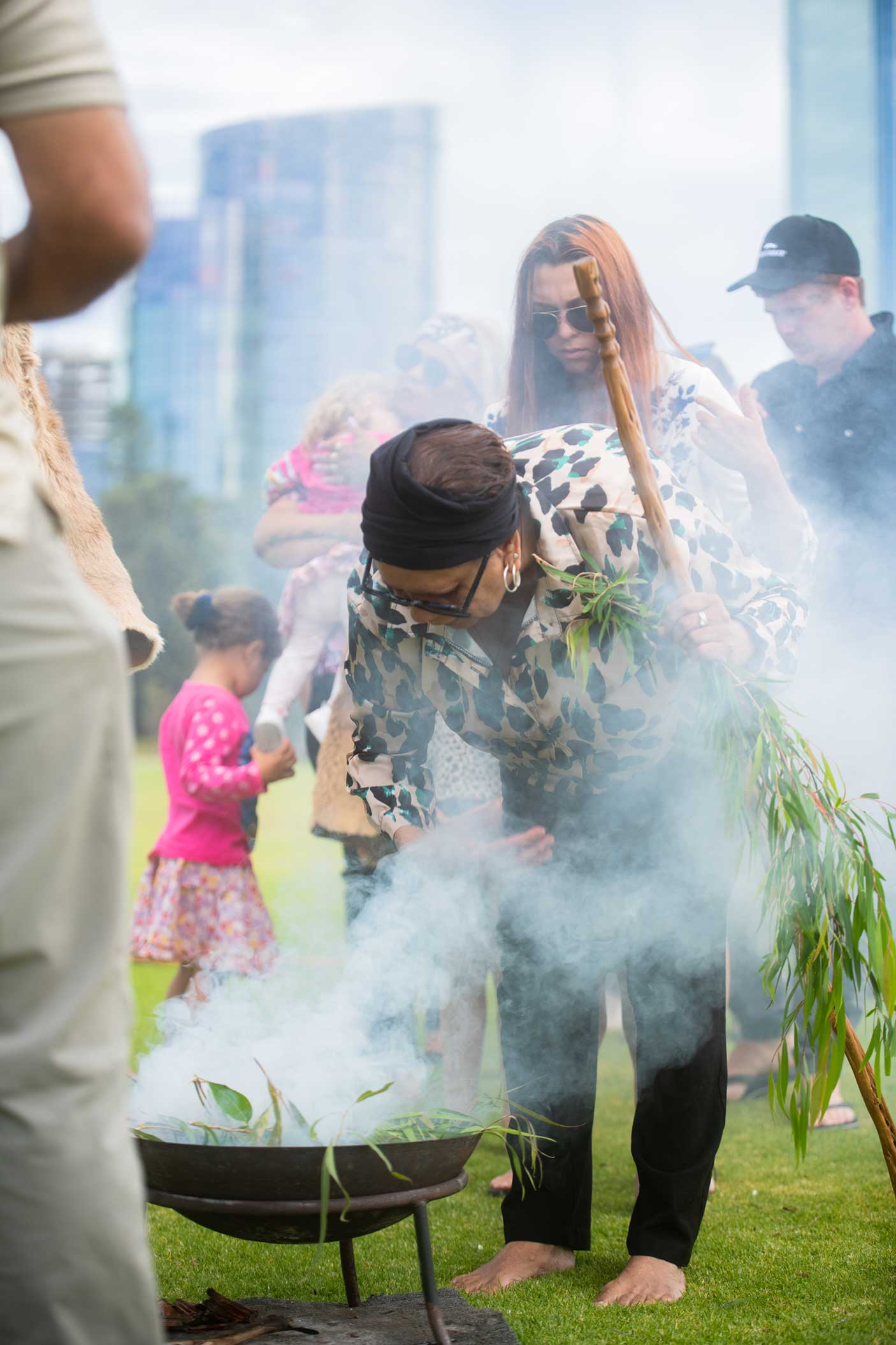 An Aboriginal women holding a stick and branch performing a cleansing ceremony