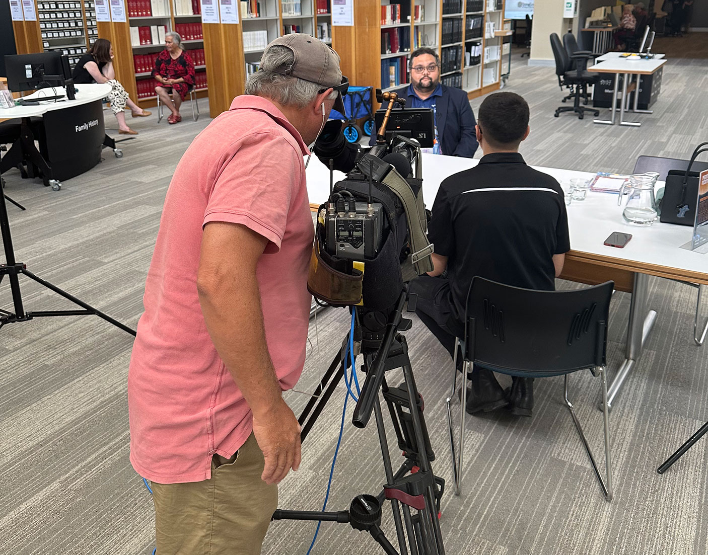 At the State Library, Community Education Officer, Duane Kelly being interviewed by Kearyn Cox from NITV.  A TV cameraman films the interview.