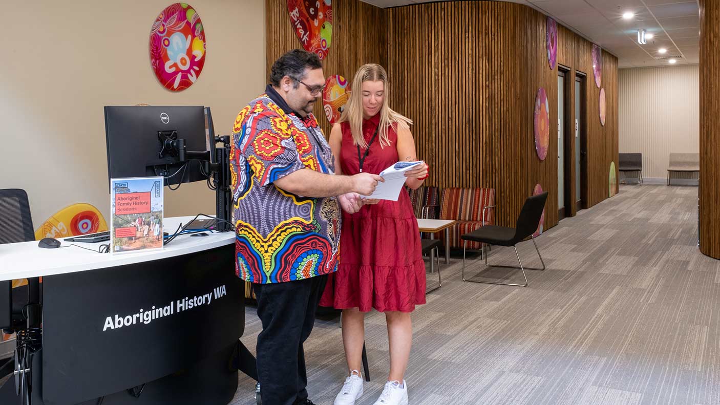 2 people in front of the Aboriginal History WA desk in a library