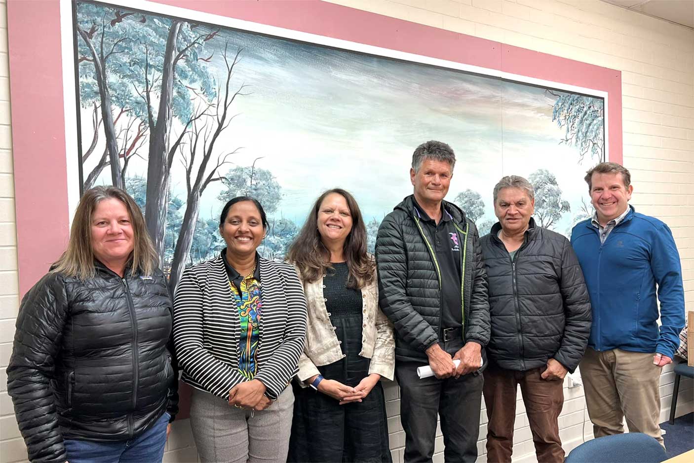 A group of people standing together in front of a painting.