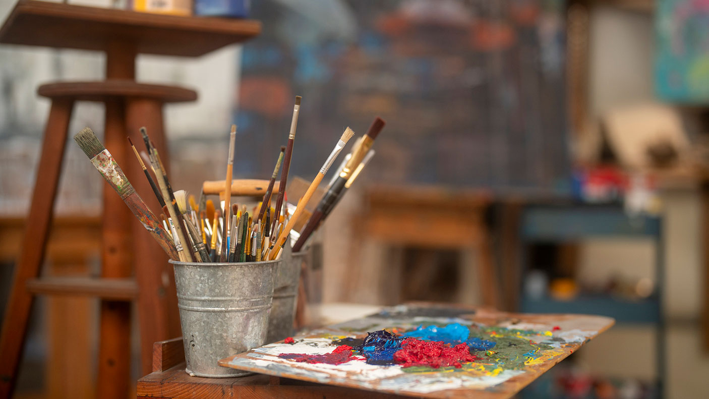 A close up an artist paint tray and brushes in a small bucket