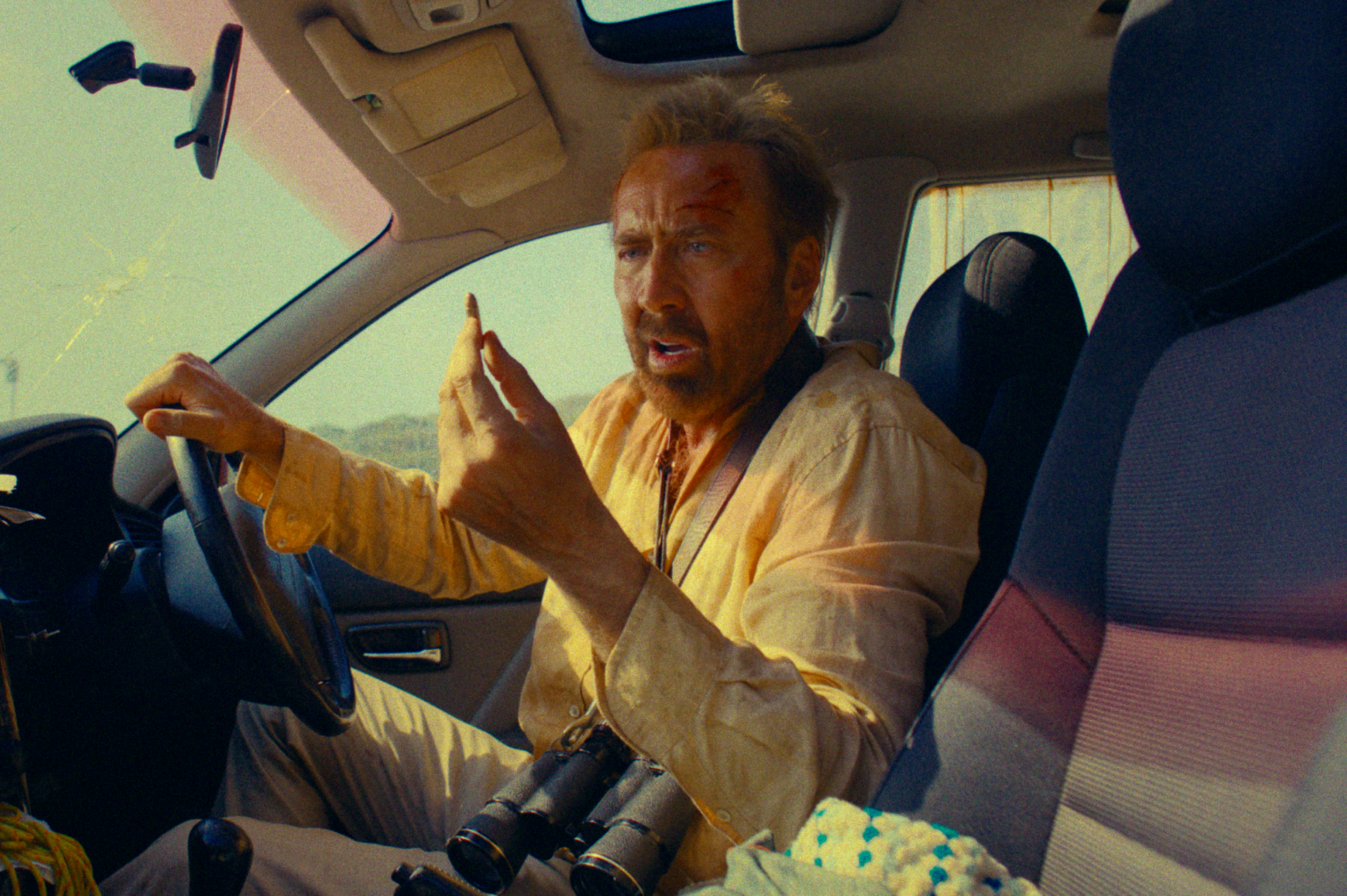 Photo of Nicolas cage driving a car in a scene from The Surfer movie.