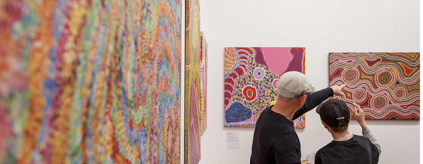 Father and son looking at Aboriginal paintings on an exhibition wall.