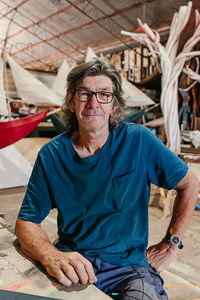 Chris Hill sitting down looking at the camera with many props behind him in his studio 