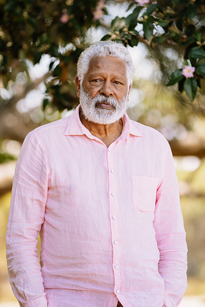 Ernie Dingo looking at the camera standing in a park under a tree
