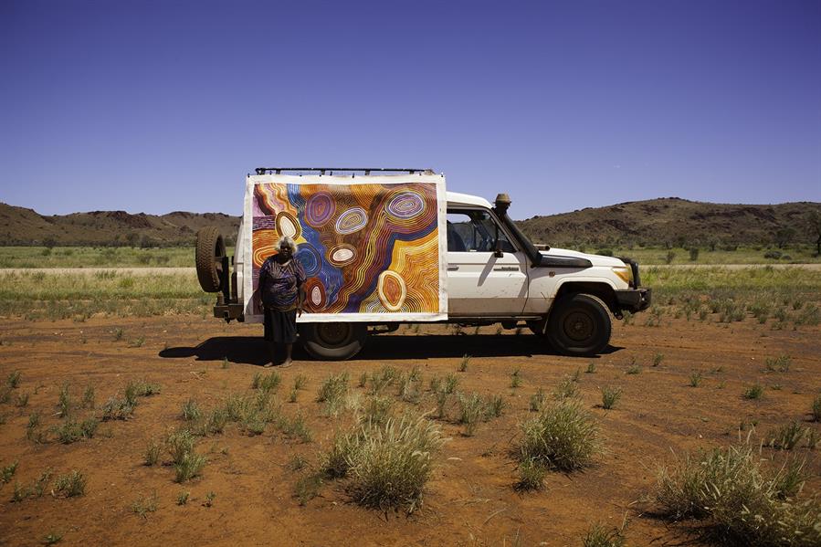 An Aboriginal artist standing in front of her artwork