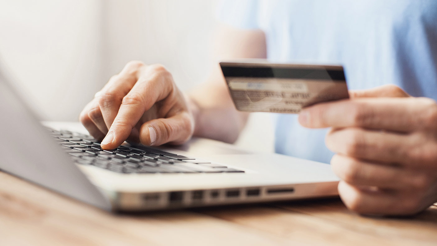 A close-up photo of someone at a laptop holding a credit card