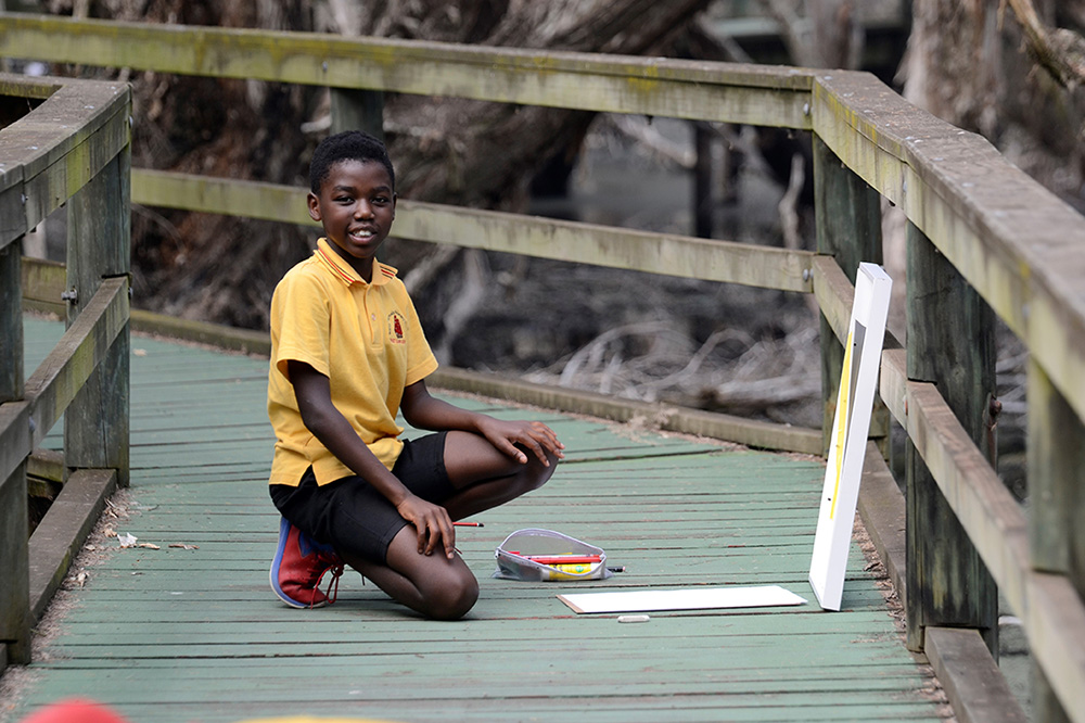 A young child kneeling down on a wooden bridge looking at a painting positioned on the ground.