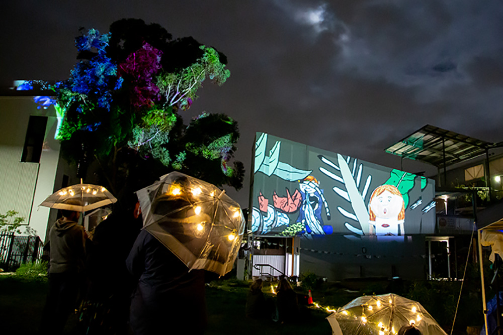 A projection on a screen at night amongst building.s.