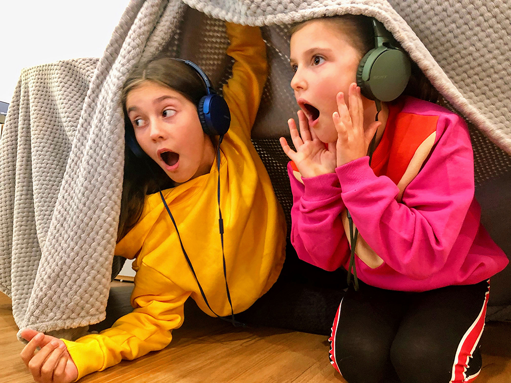 The Turners by Audioplay, 2020. Show two girls with headphones looking out of a inside cubby.