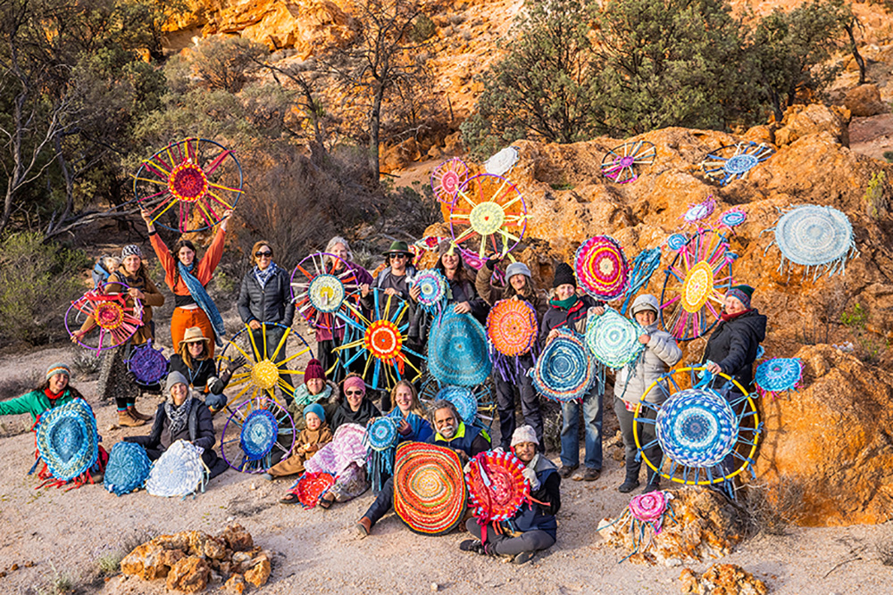A group of people holding their woven rugs near some rocks.