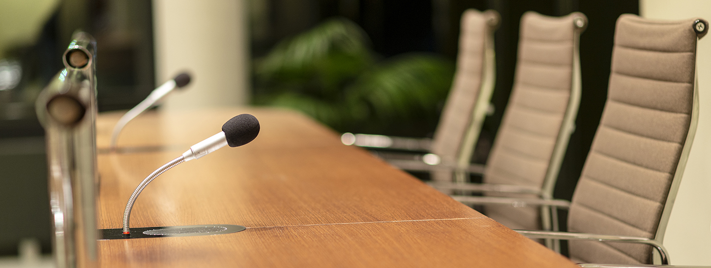 A conference desk with microphones and chairs