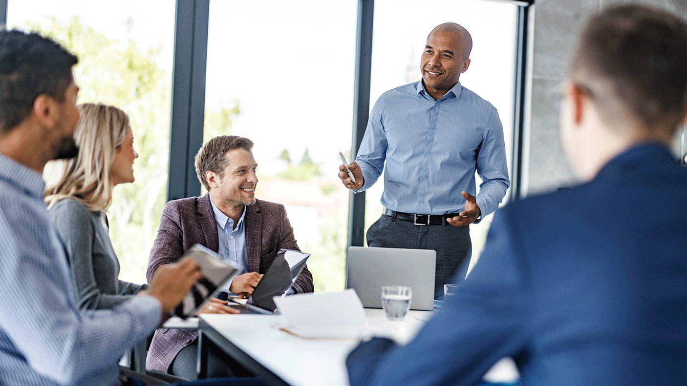 A group of people in business attire sitting at a board room table, meeting.