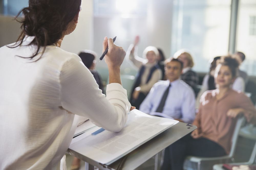 A presenter standing at a lecturn engaging an audience