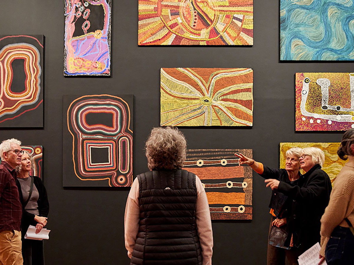 A small group of people are looking at Aboriginal art works on the wall in an art gallery