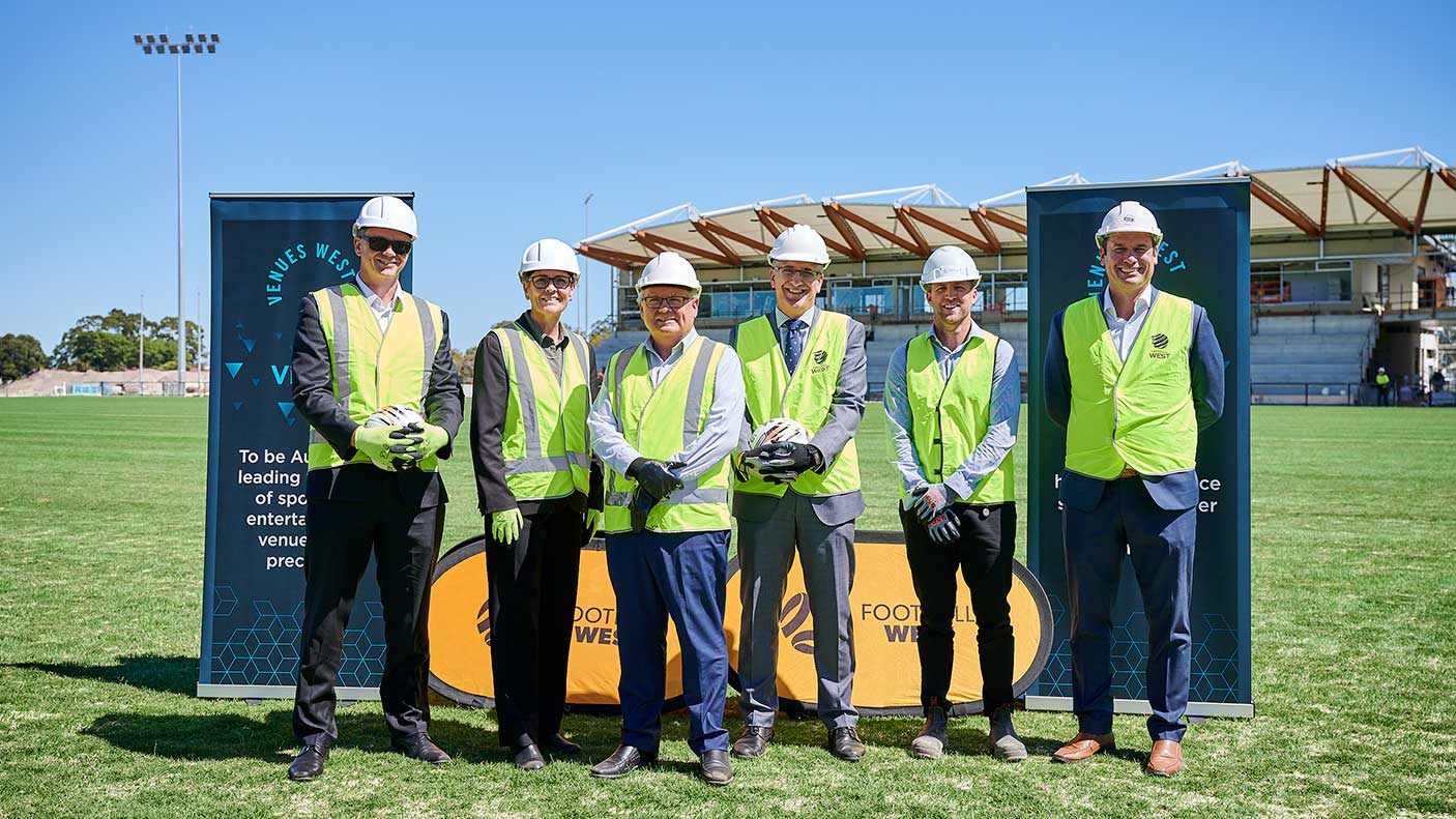 A group of people in hard hats and high vis vests standing in front on the State Football Centre.