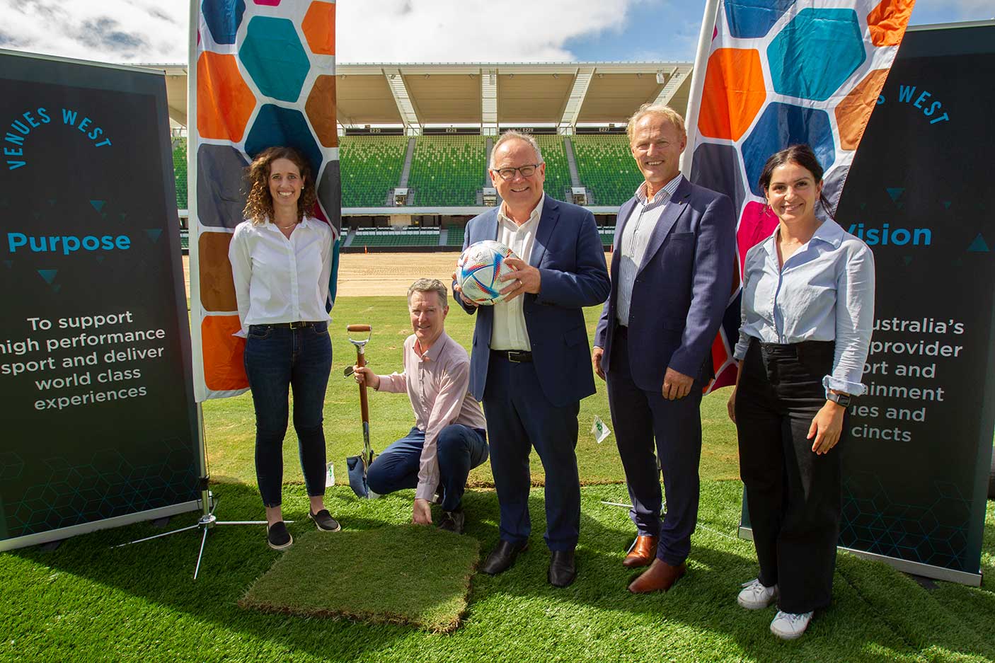 A group of people with a soccer ball and shovel on a newly laid soccer pitch