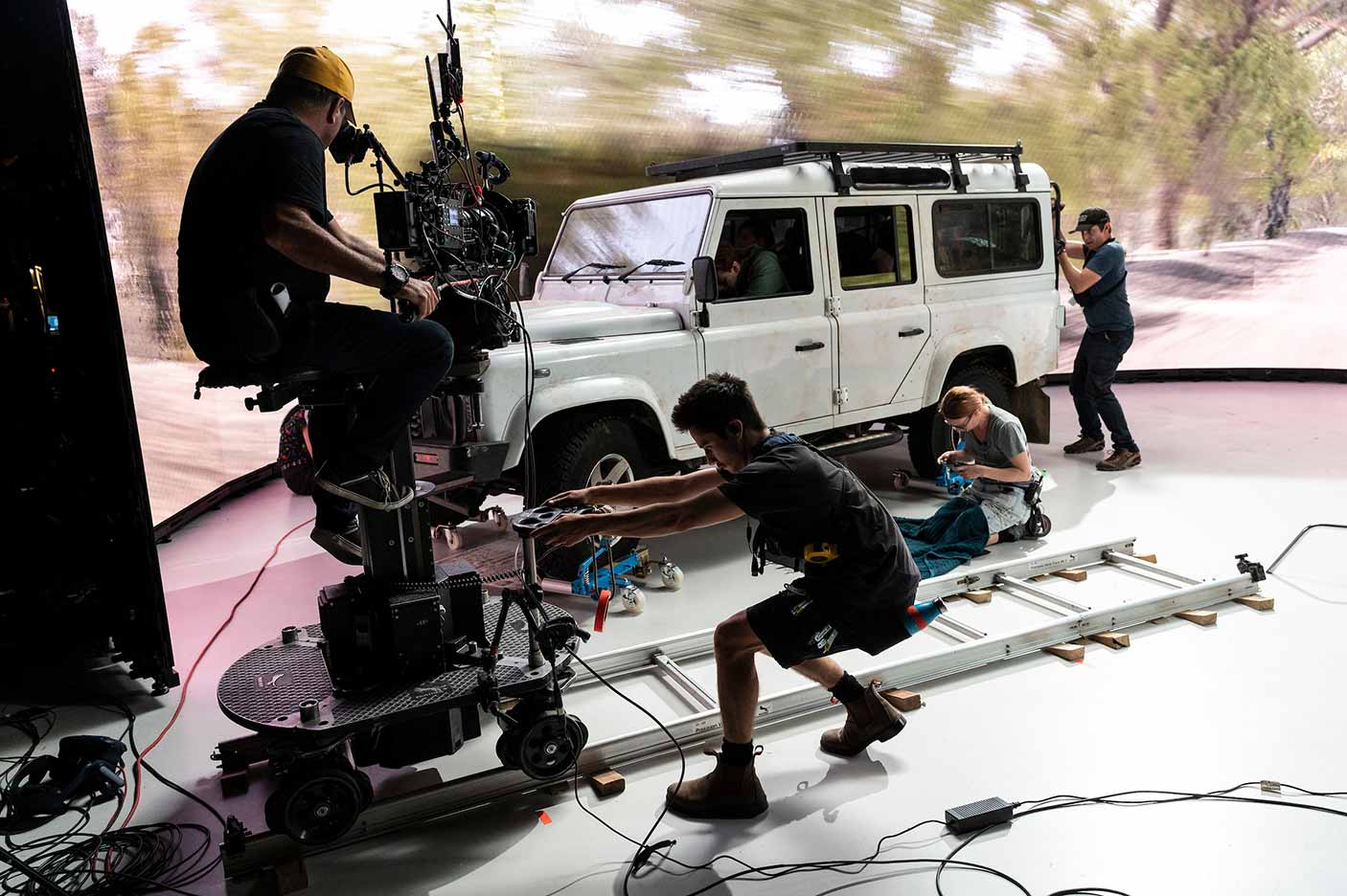 A film crew filming actors on a car inside a studio