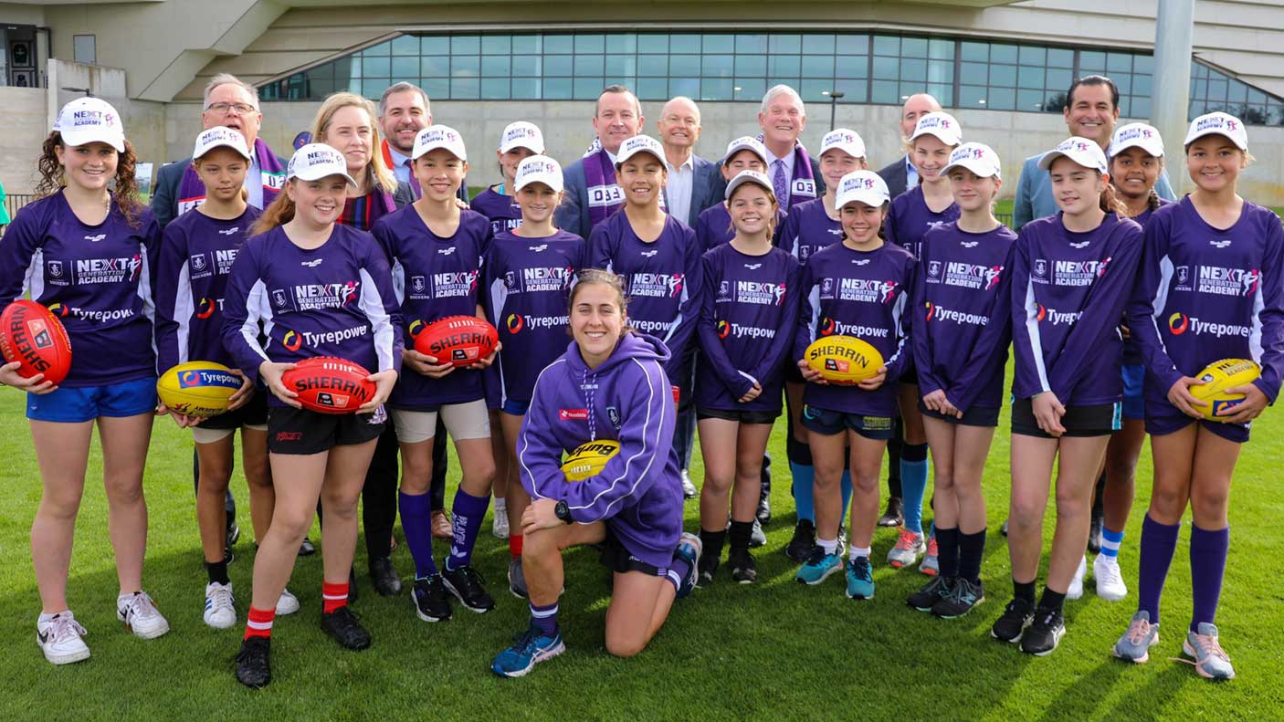 Female football players standing in a group in Fremantle colours with the Premier, Ministers, Mayor and officials.