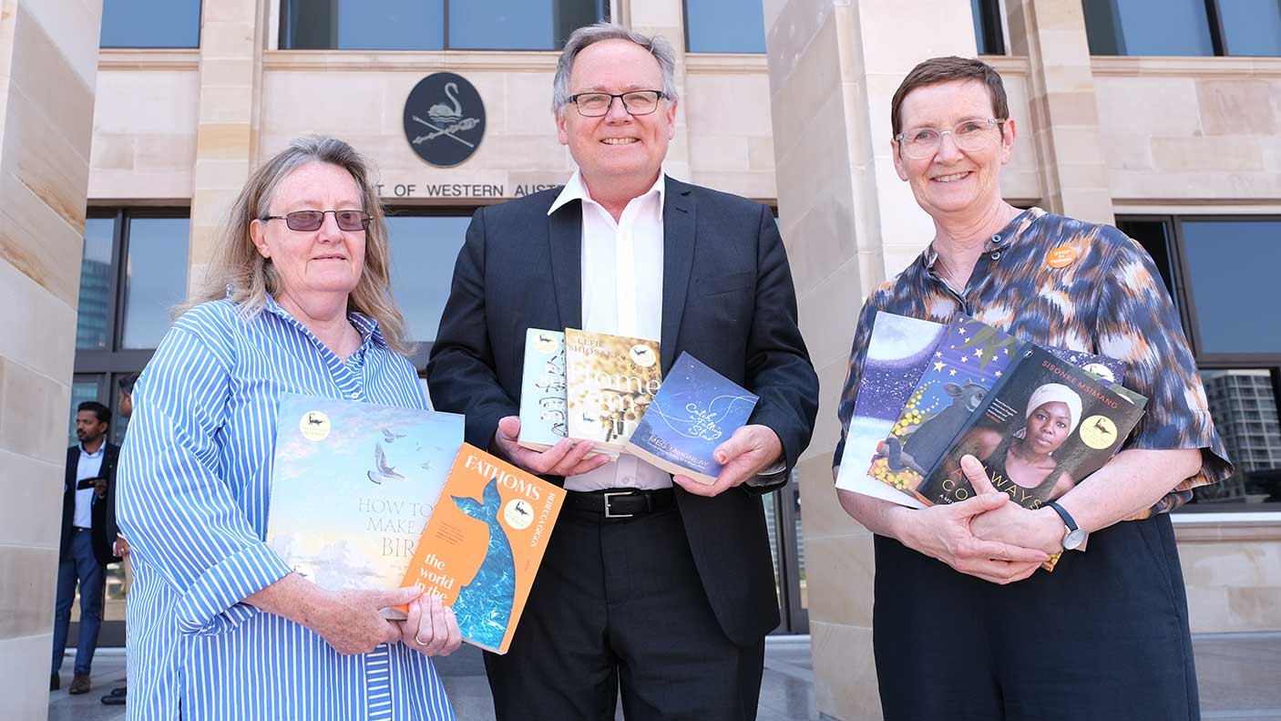 3 people standing outside of Parliament holding books.