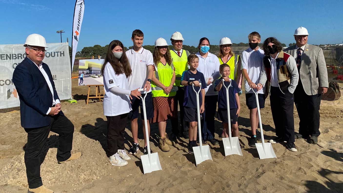 A group of people, including kids, holding shovels in an empty patch of dirt