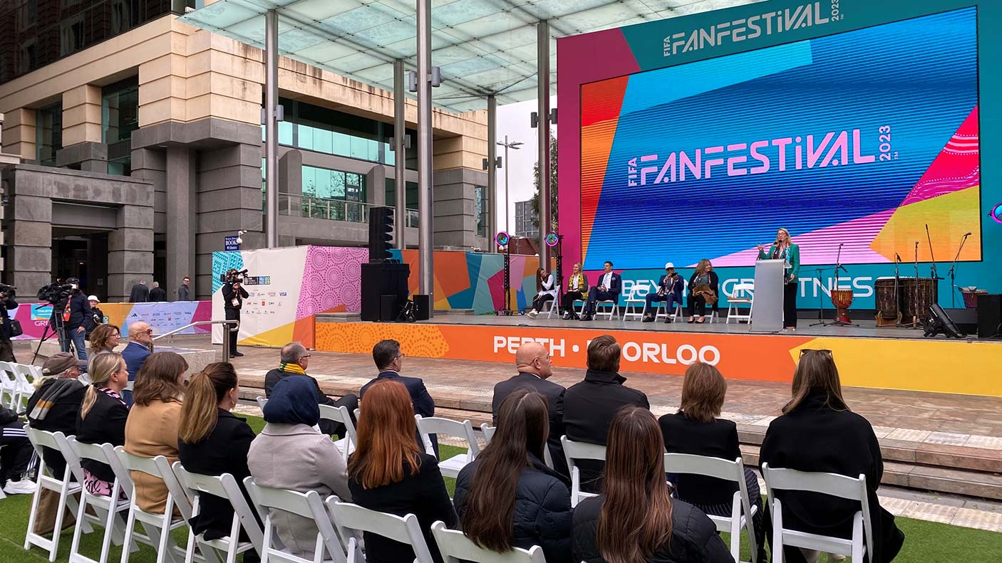 A seated audience listening to a speak on stage in Forrest Place, Perth with a large screen in the brand colours of the FIFA Women's World Cup.