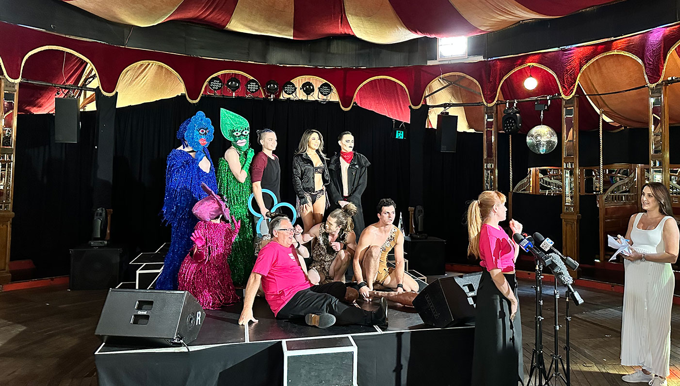 Minister Templeman and a group colourful performers on the stage of a circus tent