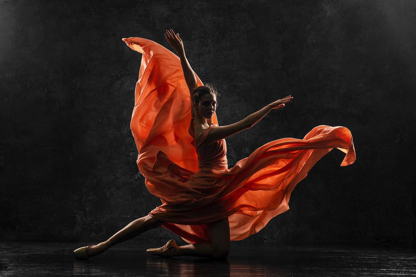 Silhouette photo of a young ballet dancer dressed in a long peach dress, pointe shoes with ribbons.