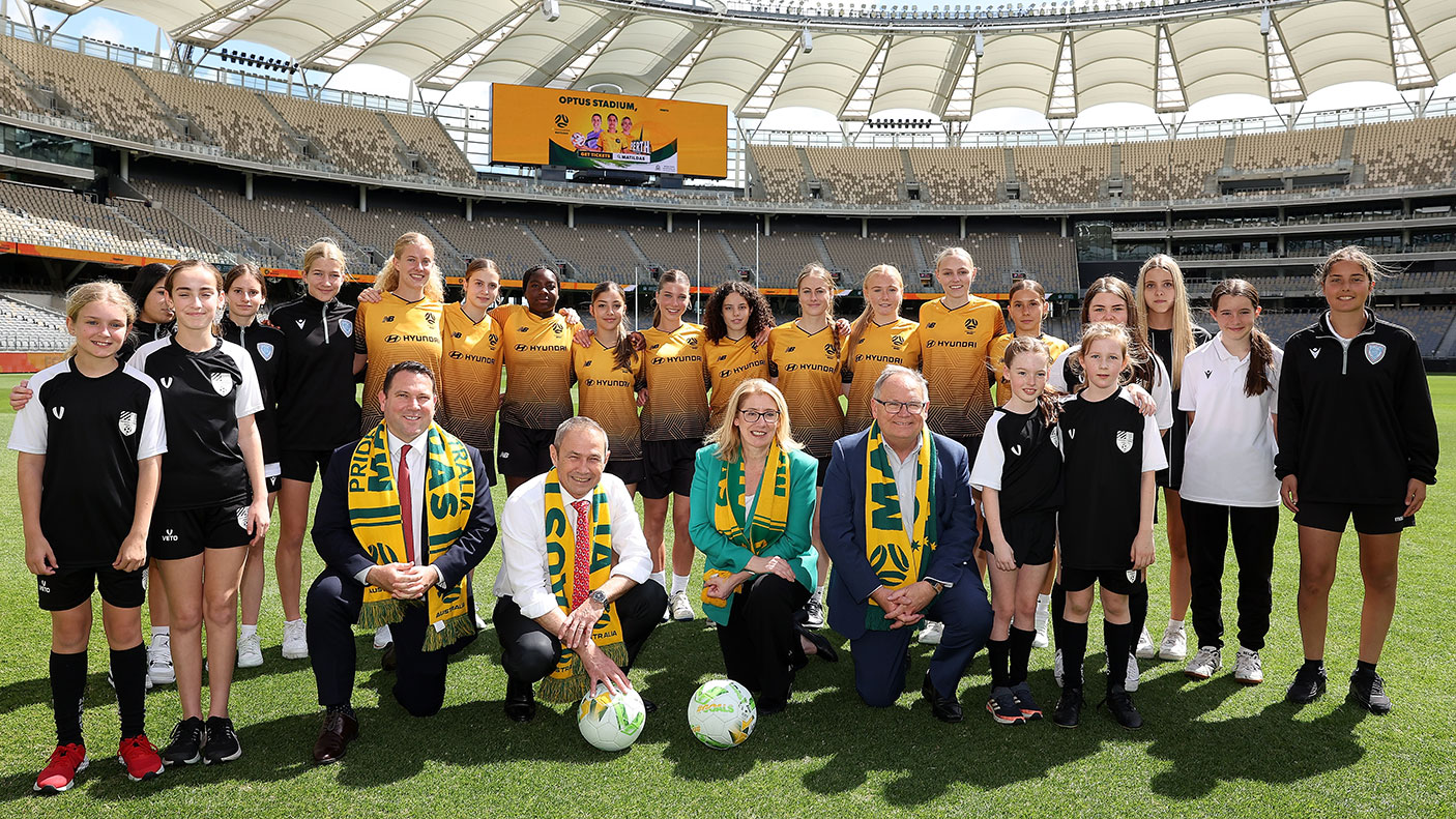 A large group of people standing together on the pitch of Optus Stadium at the Matildas Optus Stadium media announcement