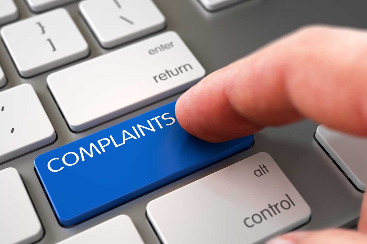 A close up photo of someone pressing a key on a keyboard with the word, 'complaint' on it