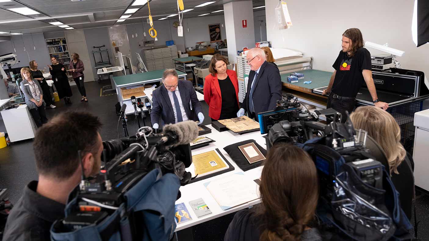 A group of people with media around desk with item from the collection