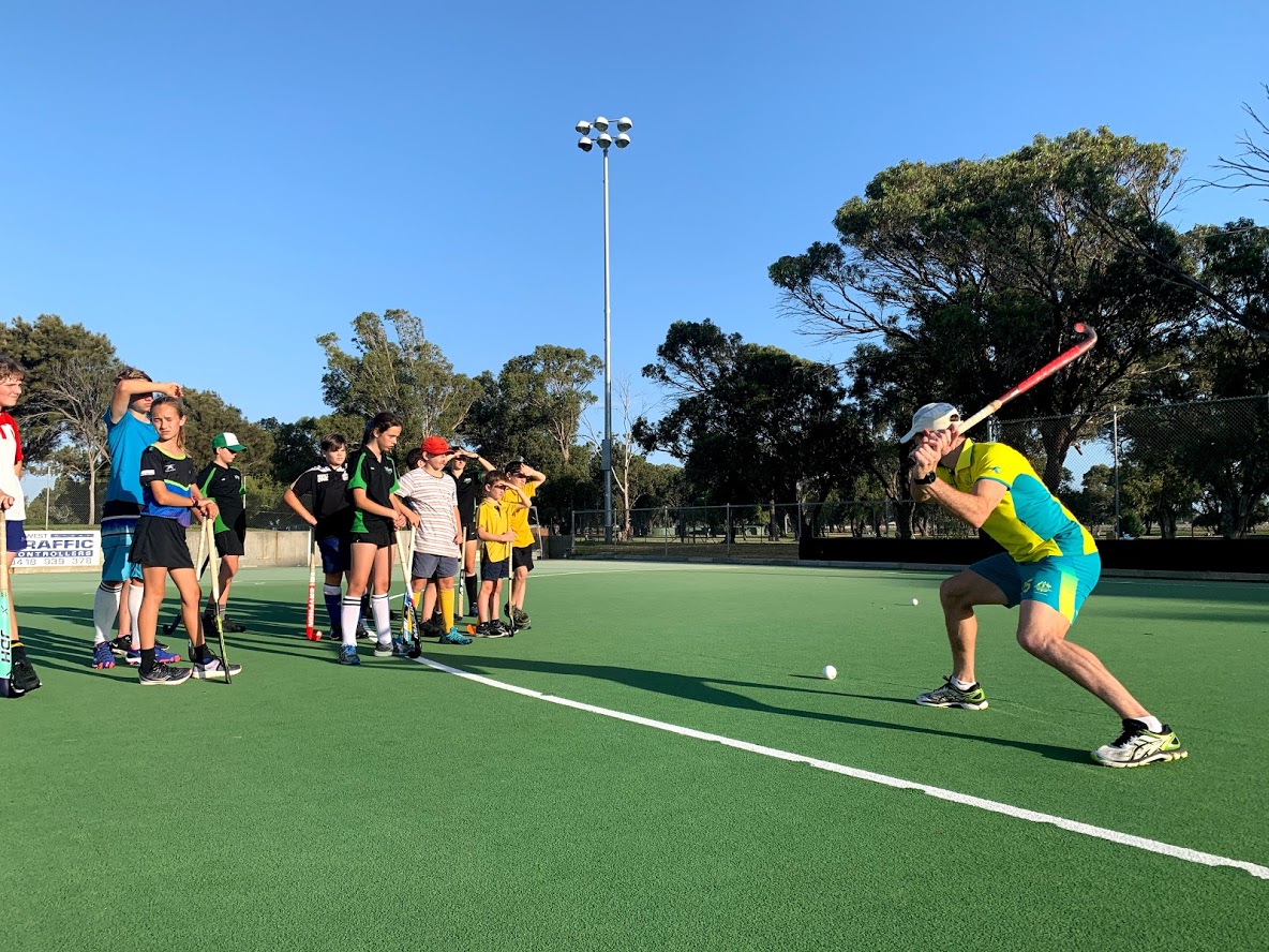 A hockey player demonstrating hitting the ball in front of children