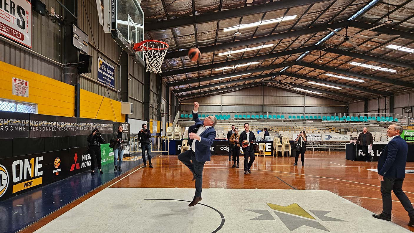 Minister David Templeman shooting the basketball towards the hoop with people watching.