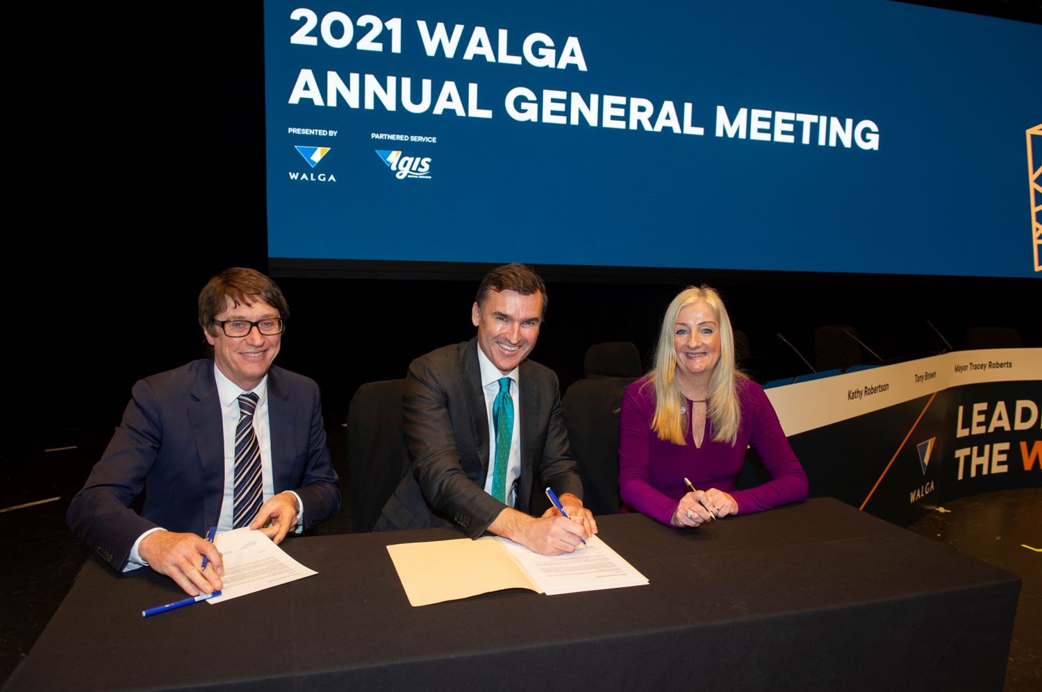 Three people signing a document, seated at a desk