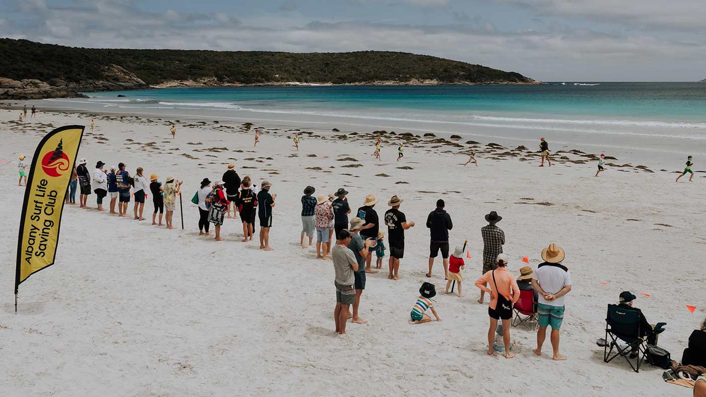 A line of people on a beach looking out to the surf.