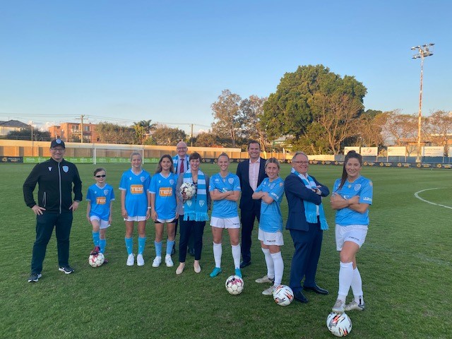 A group of people, most in football uniforms, standing on a football (soccer) pitch