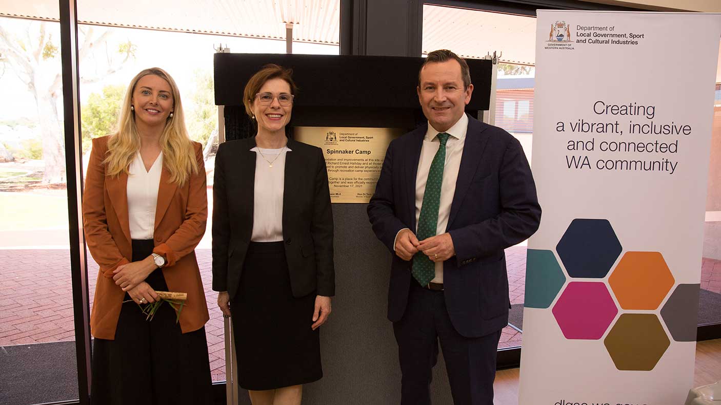 Three people standing in front of a plaque for the opening of the Spinnaker precinct at Ern Halliday Recreation Camp.