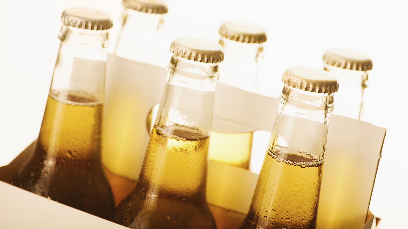 Close up image of 6 bottle of beer with caps on, in a cardboard carry box