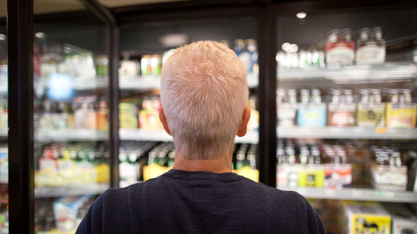 Mature man hesitates while picking out beer from a store.