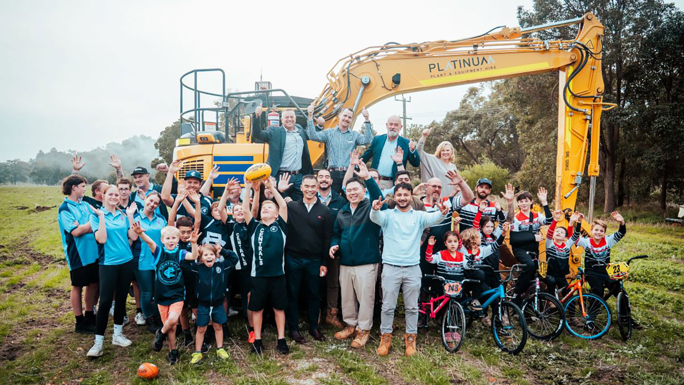 A group of community members stand next to  large construction machinery