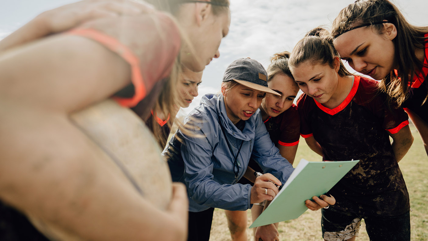A group of sports people huddle around a coach, who is holding apiece of paper