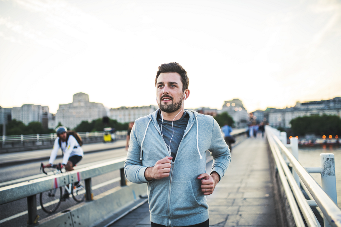 Young sporty man with earphones running on the bridge outside in a city. - stock photo