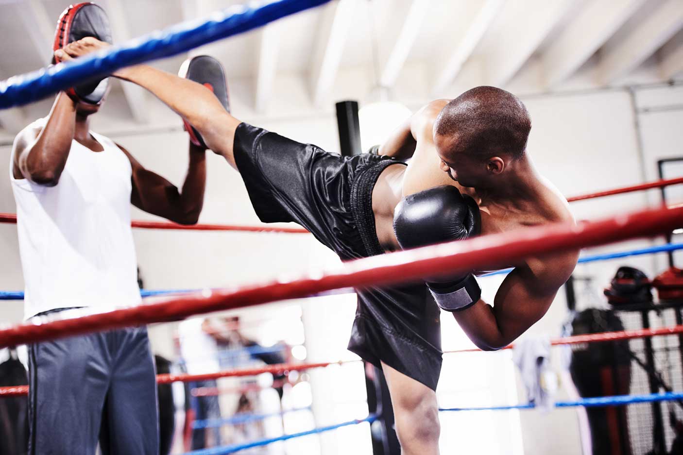 A kickboxer launching a high kick at his sparring partner's gloves
