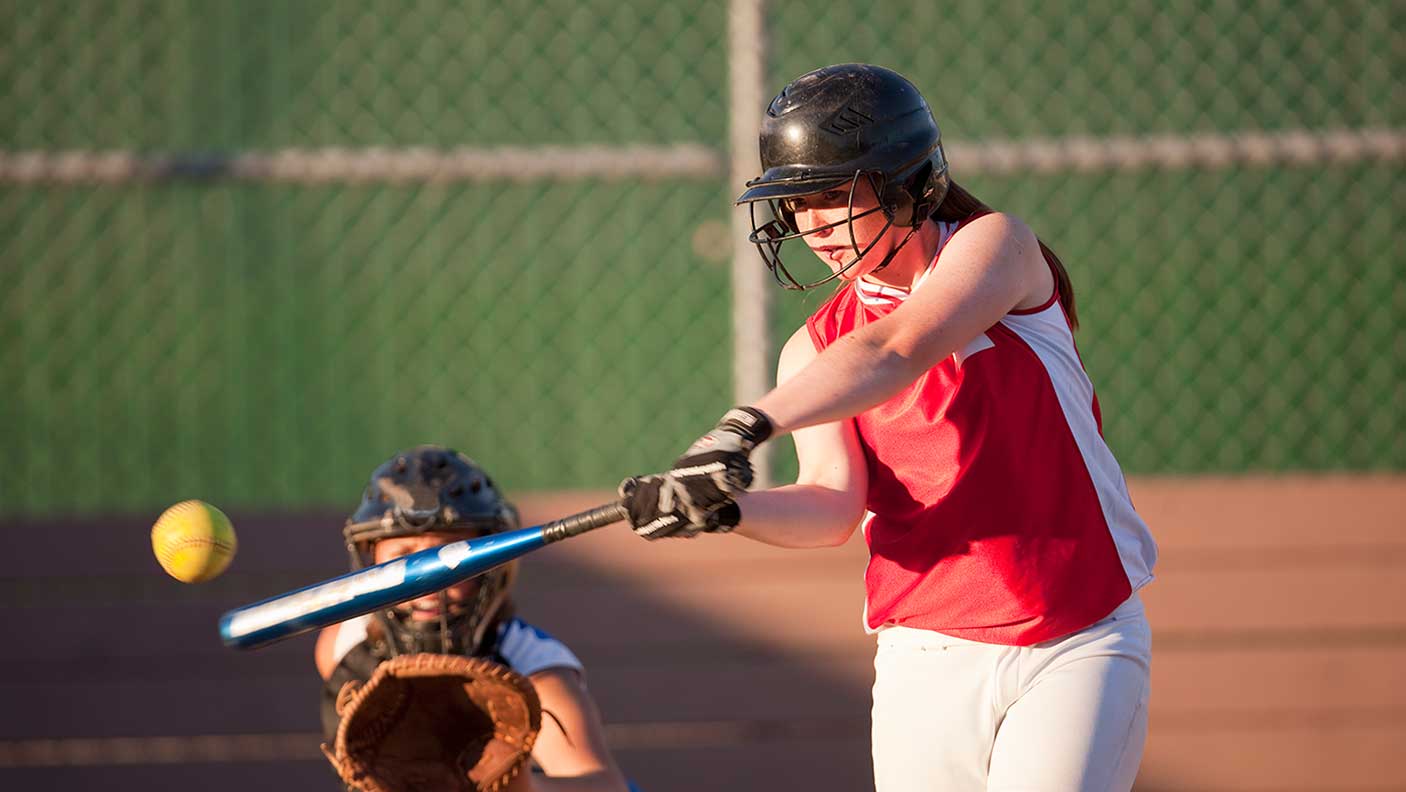 Softball player hits softball while batting