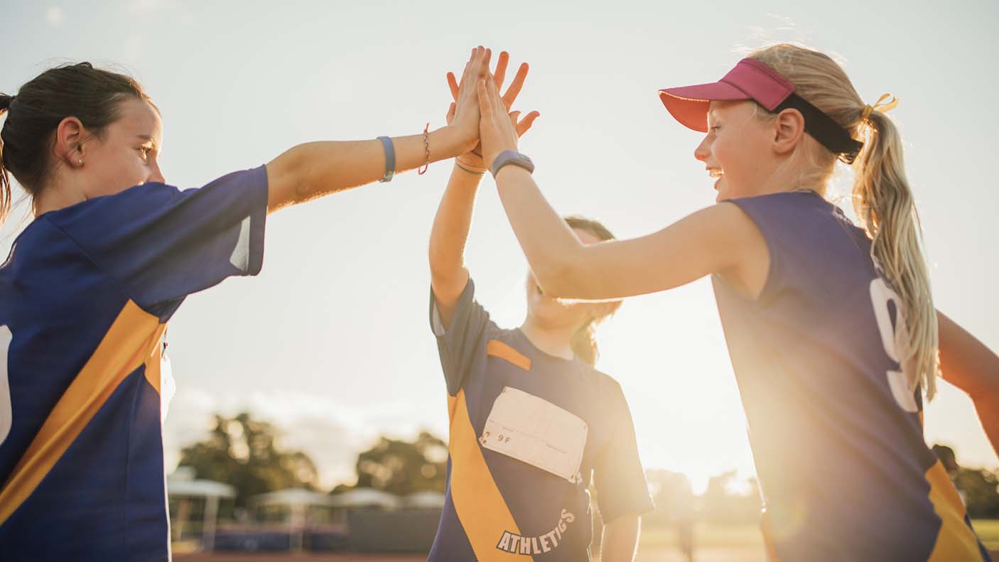 Three girls are high-fiving after a race at athletics club.