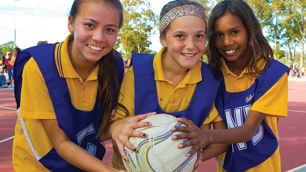 Three junior netballers holding a netbal