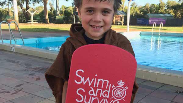 A child in front of a pool holding a kick board