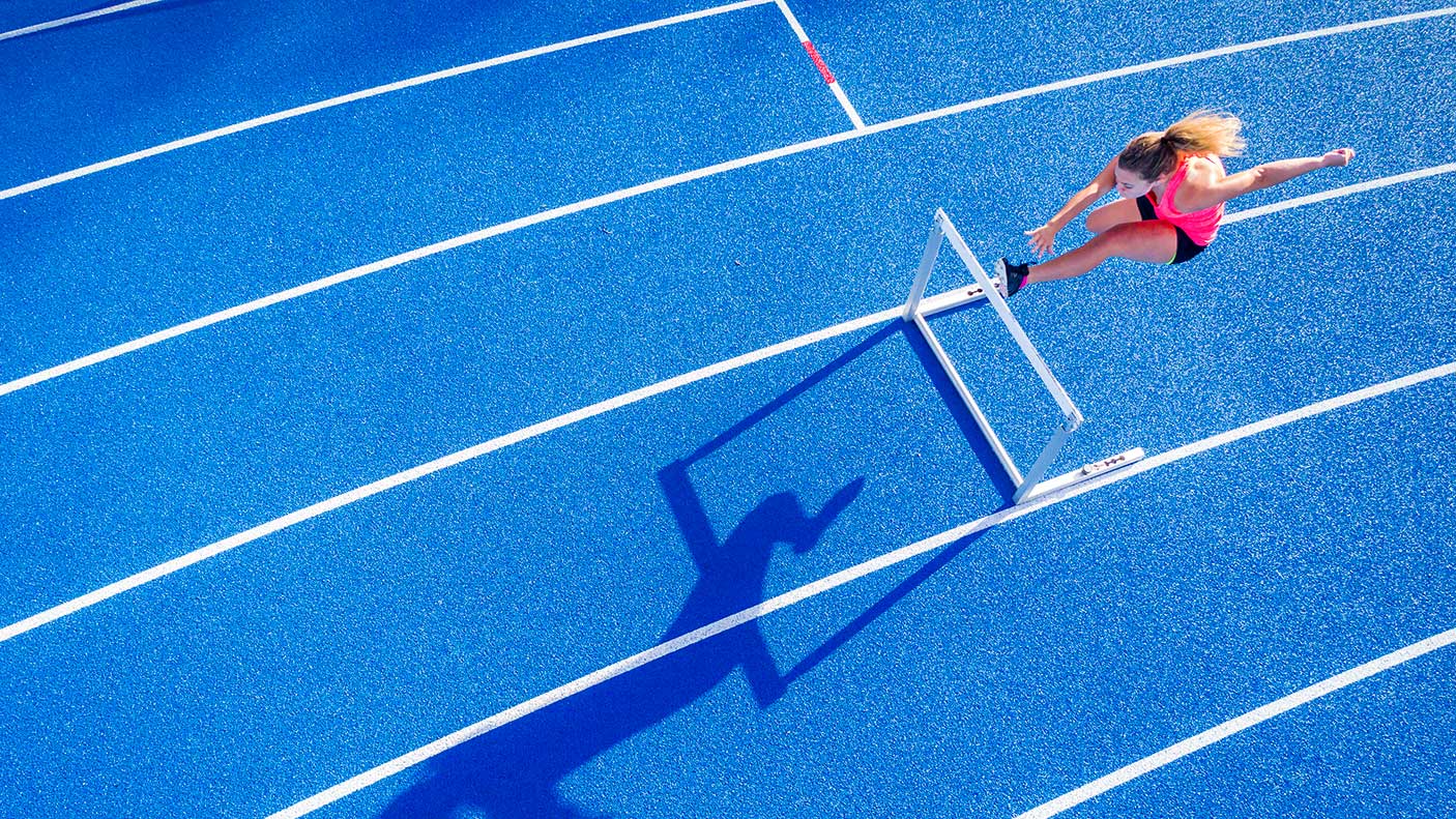 Top view of female runner crossing hurdle on tartan track